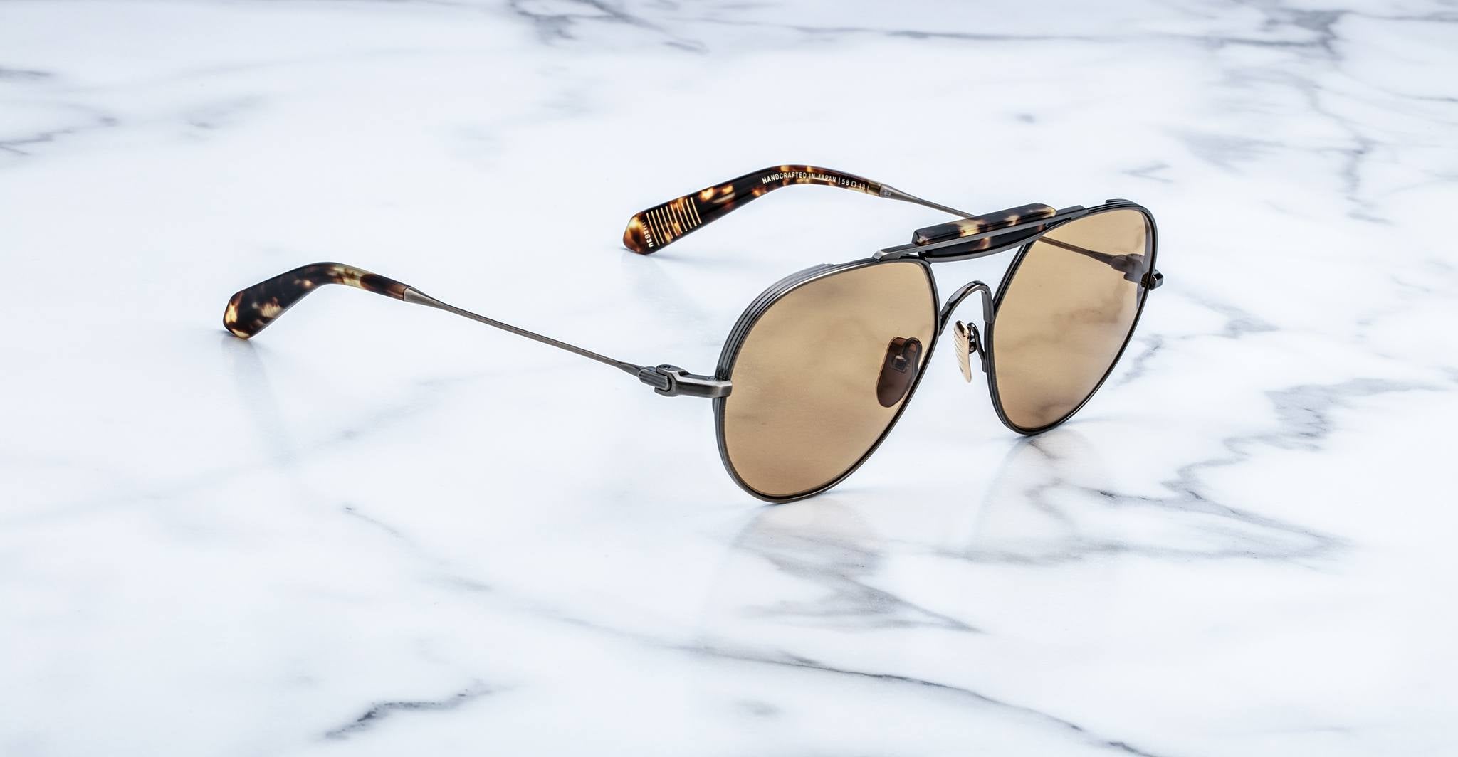 A pair of aviator-style sunglasses with brown lenses and tortoiseshell-patterned arms, resting on a white marble surface.