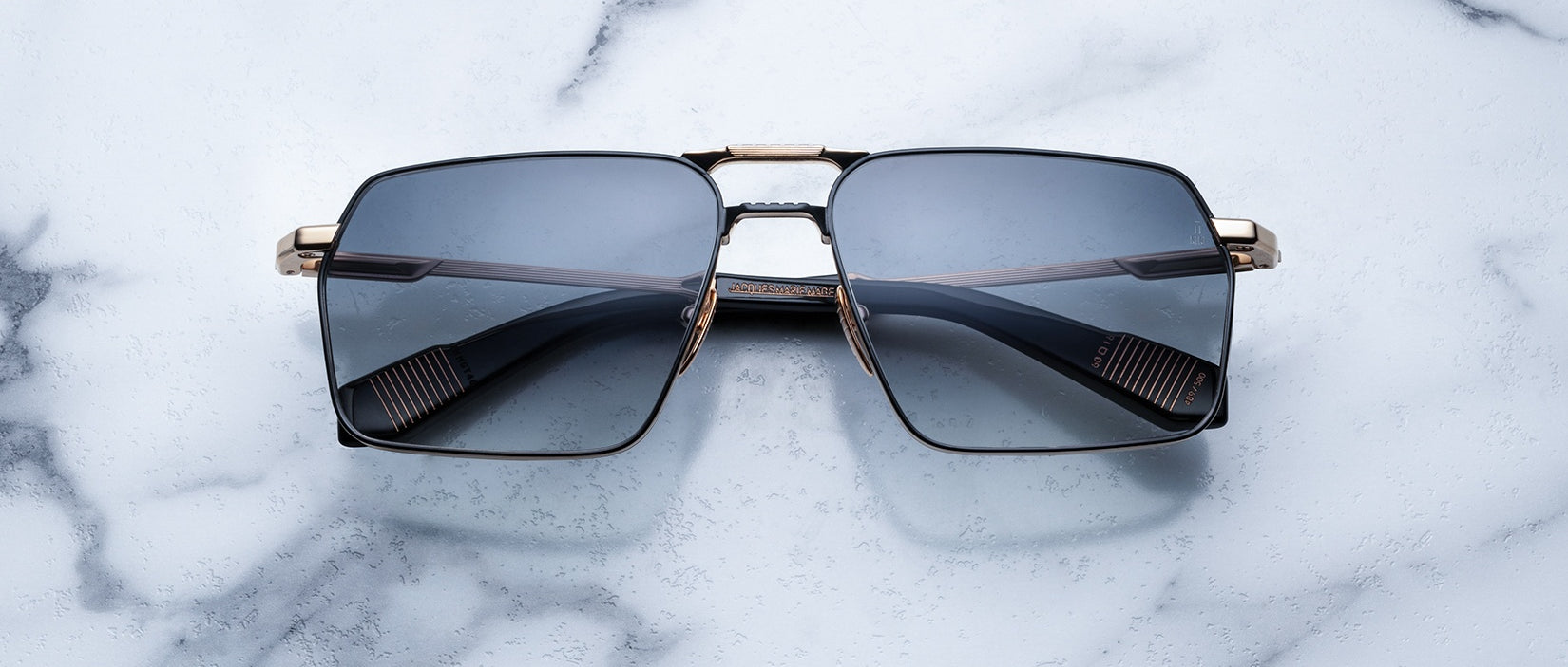 Rectangular sunglasses with dark tinted lenses and gold metal frames resting on a white marble surface.