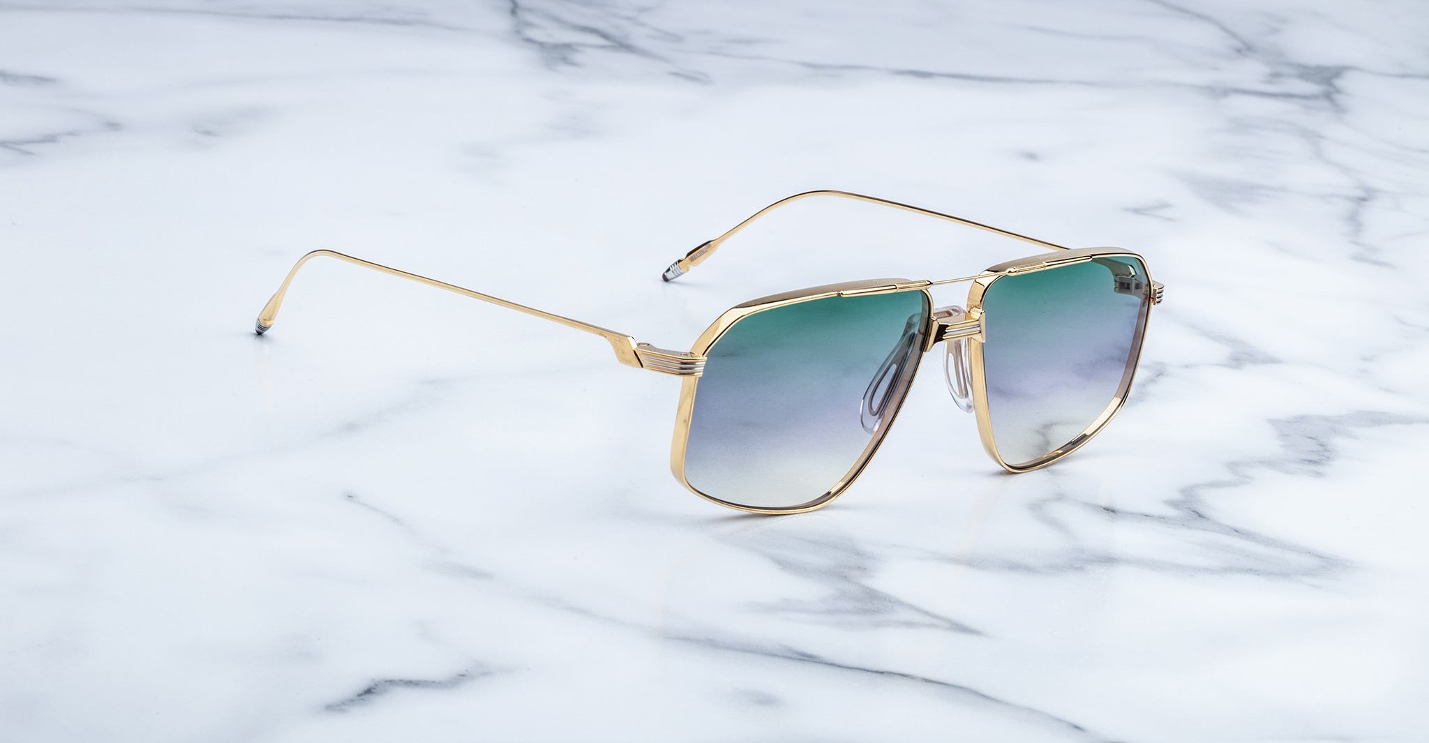 Jacques Marie Mage Jagger oversized aviator sunglasses, featuring gold frames and green gradient lenses, from Jacques Marie Mage, rest on a sleek white marble surface.