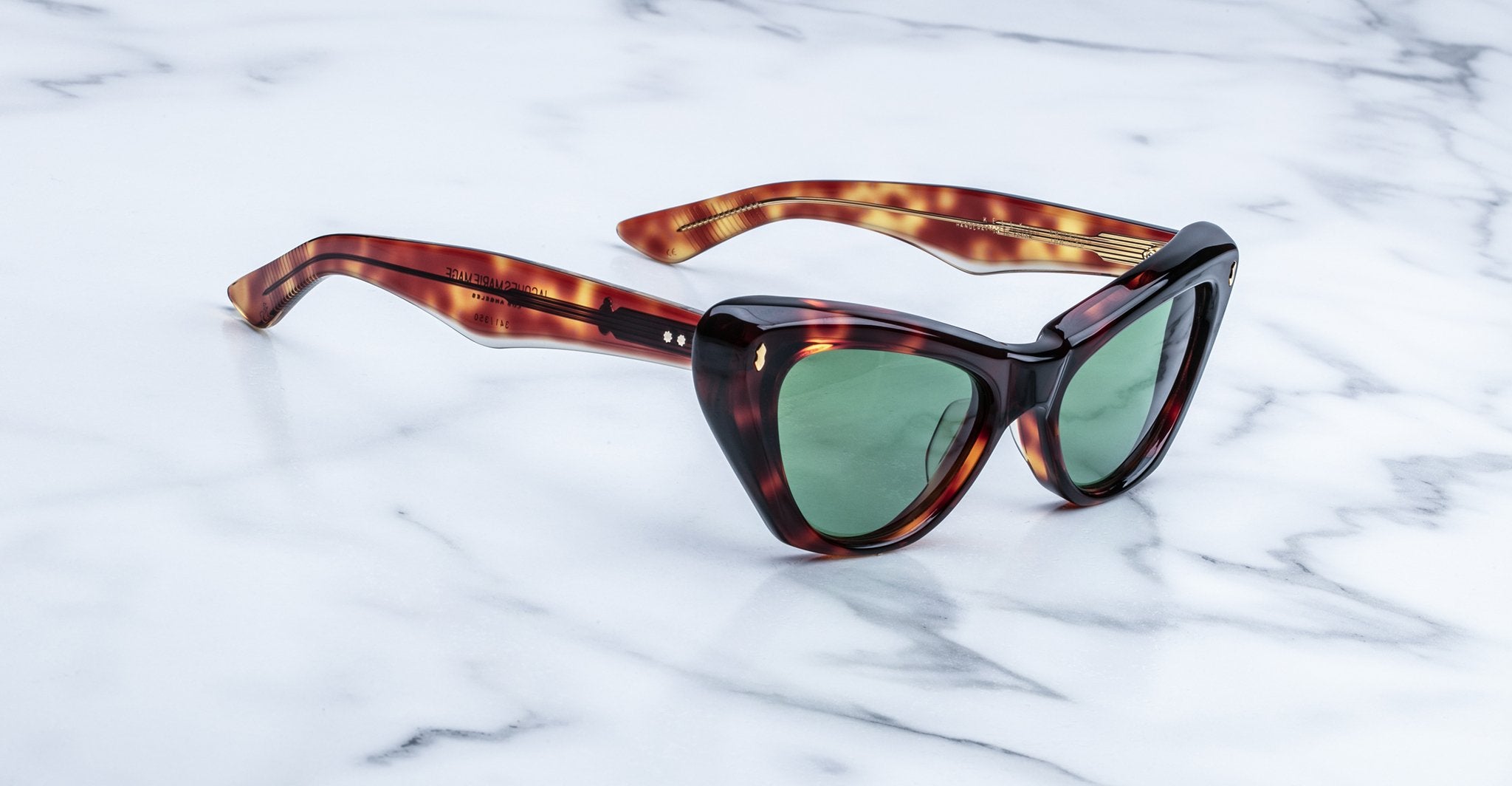 A pair of tortoiseshell cat-eye sunglasses with green lenses is placed on a white marble surface.