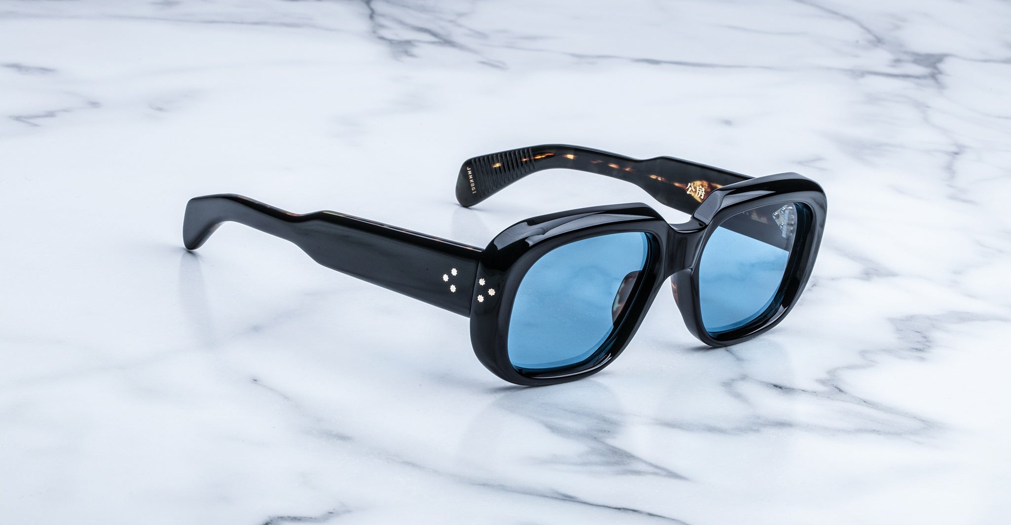 Jacques Marie Mage Kobo sunglasses with black frames and blue lenses, top view.