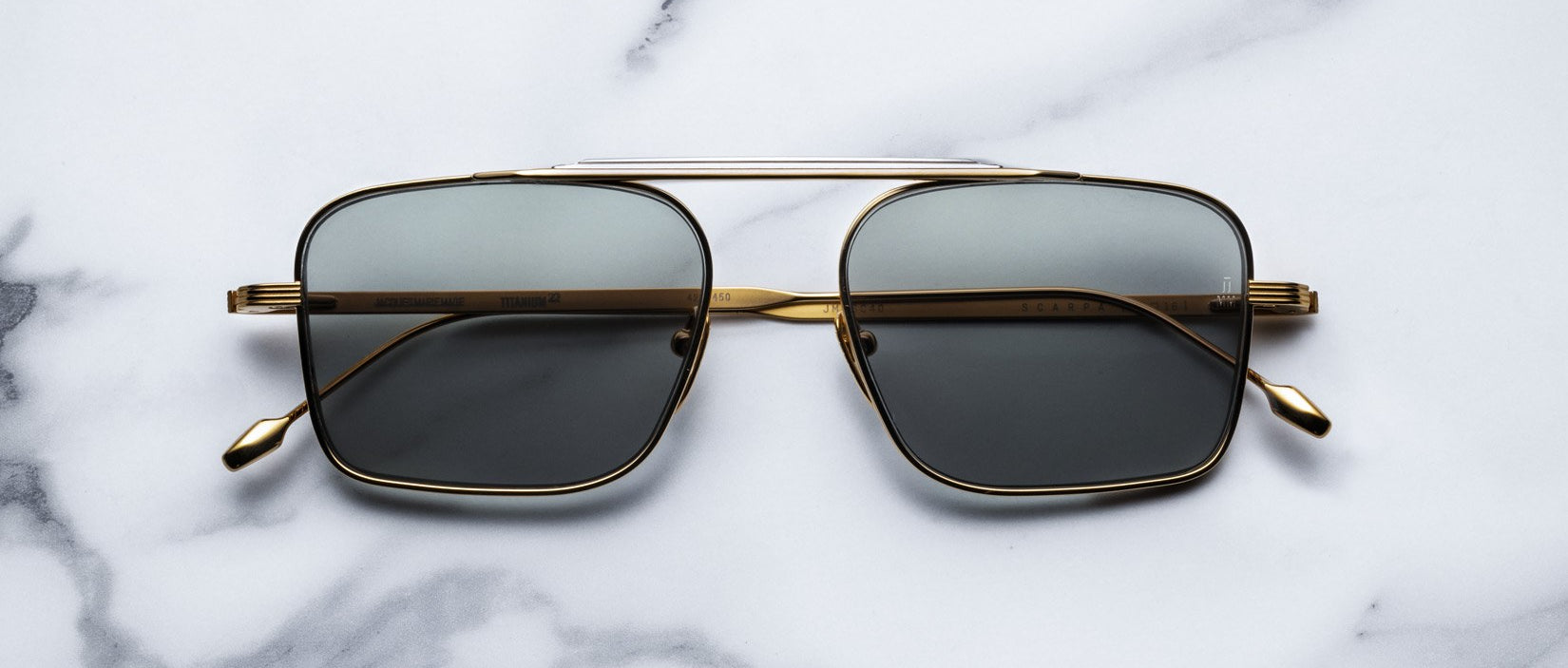 Gold-framed aviator sunglasses with dark lenses placed on a white marble surface.
