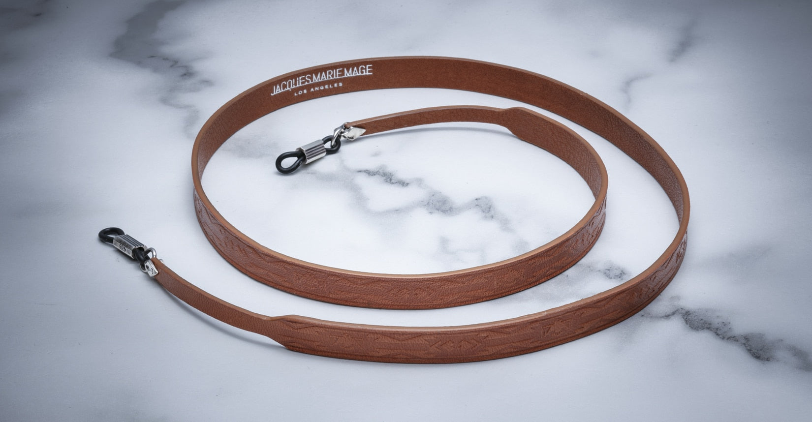 Jacques Marie Mage Strap Tooled camera strap, brown leather with metal clips, product shown coiled, top view.