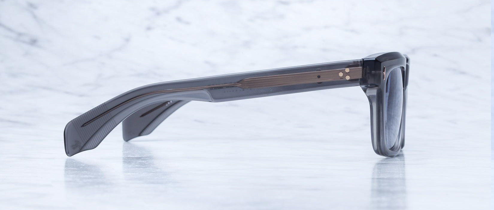 The Jacques Marie Mage Torino bold rectangular eyeglass frames by Jacques Marie Mage rest on a light gray marble surface, highlighting their handcrafted acetate construction and elegant temples.