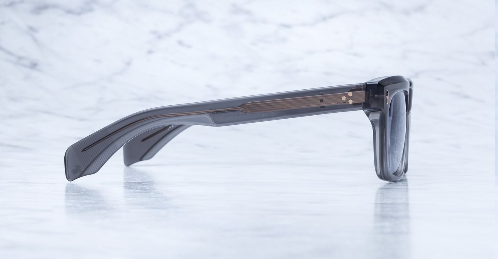 The Jacques Marie Mage Torino bold rectangular eyeglass frames by Jacques Marie Mage rest on a light gray marble surface, highlighting their handcrafted acetate construction and elegant temples.