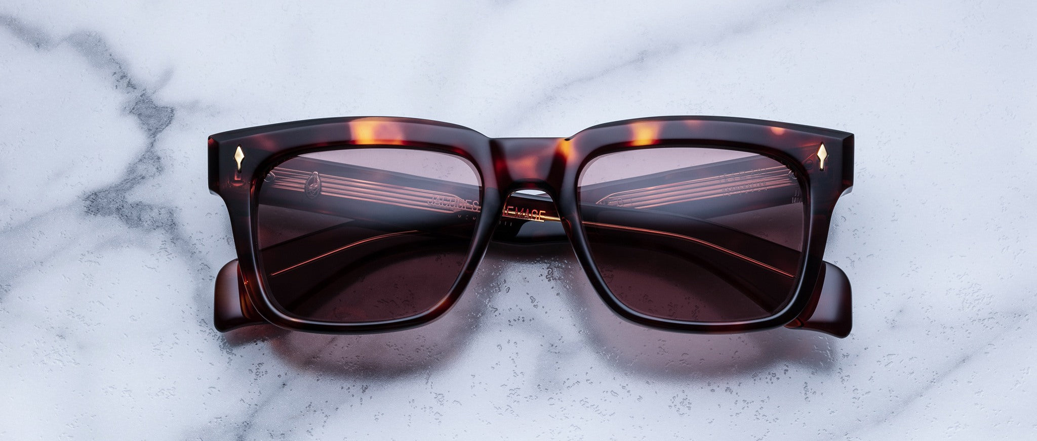 Jacques Marie Mage Torino sunglasses with bold square tortoiseshell frames and dark lenses rest on a white marble surface, showcasing the handcrafted acetate style of Jacques Marie Mage.