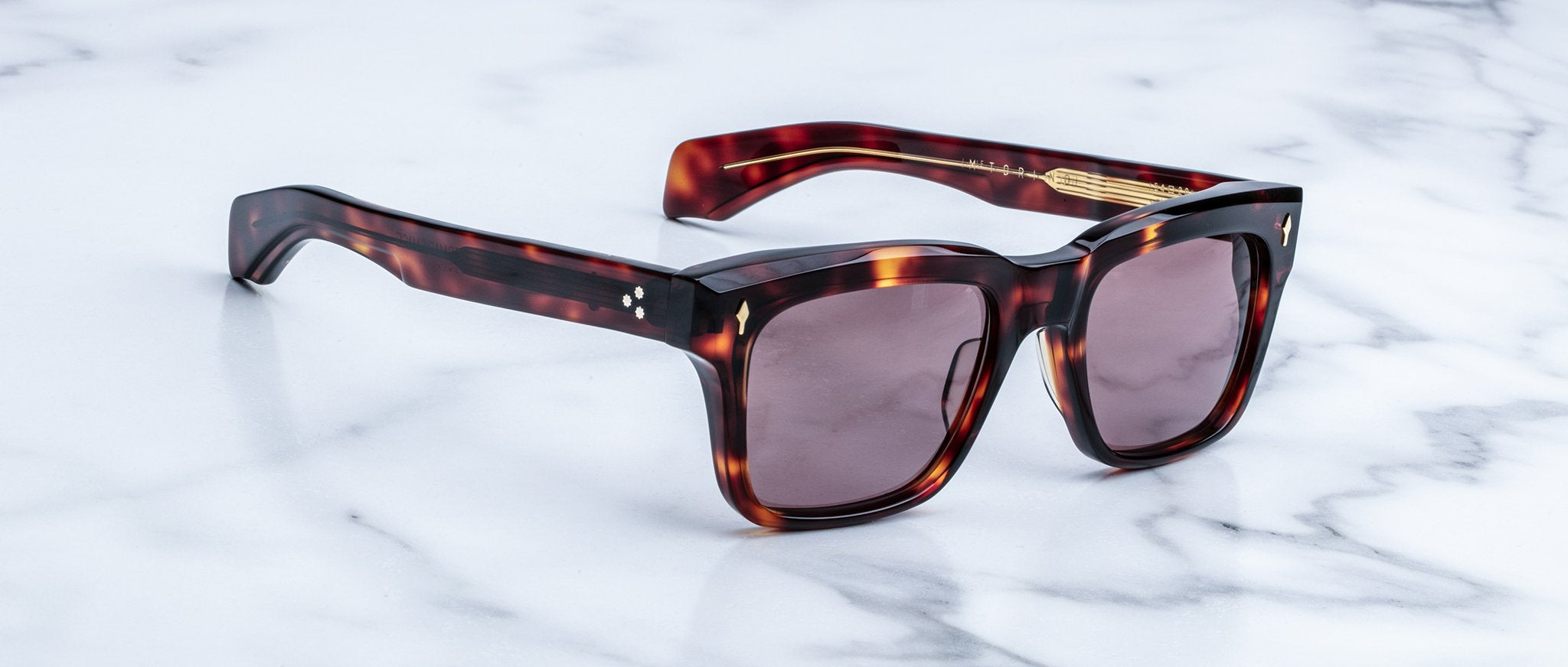 The Jacques Marie Mage Torino sunglasses by Jacques Marie Mage feature tortoiseshell rectangular frames and dark lenses, inspired by bold eyeglass designs, and are displayed elegantly on a white marble surface.