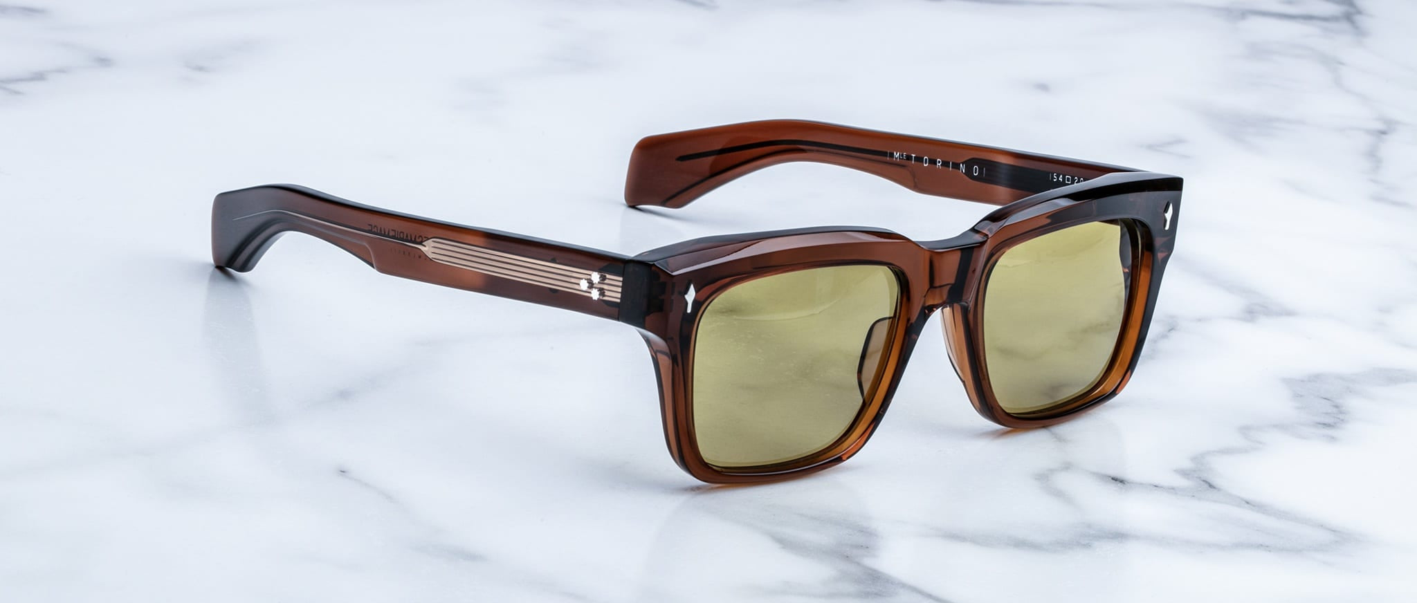 Jacques Marie Mage Torino sunglasses: brown square frames in handcrafted acetate with yellow-tinted lenses, styled on a white marble surface.