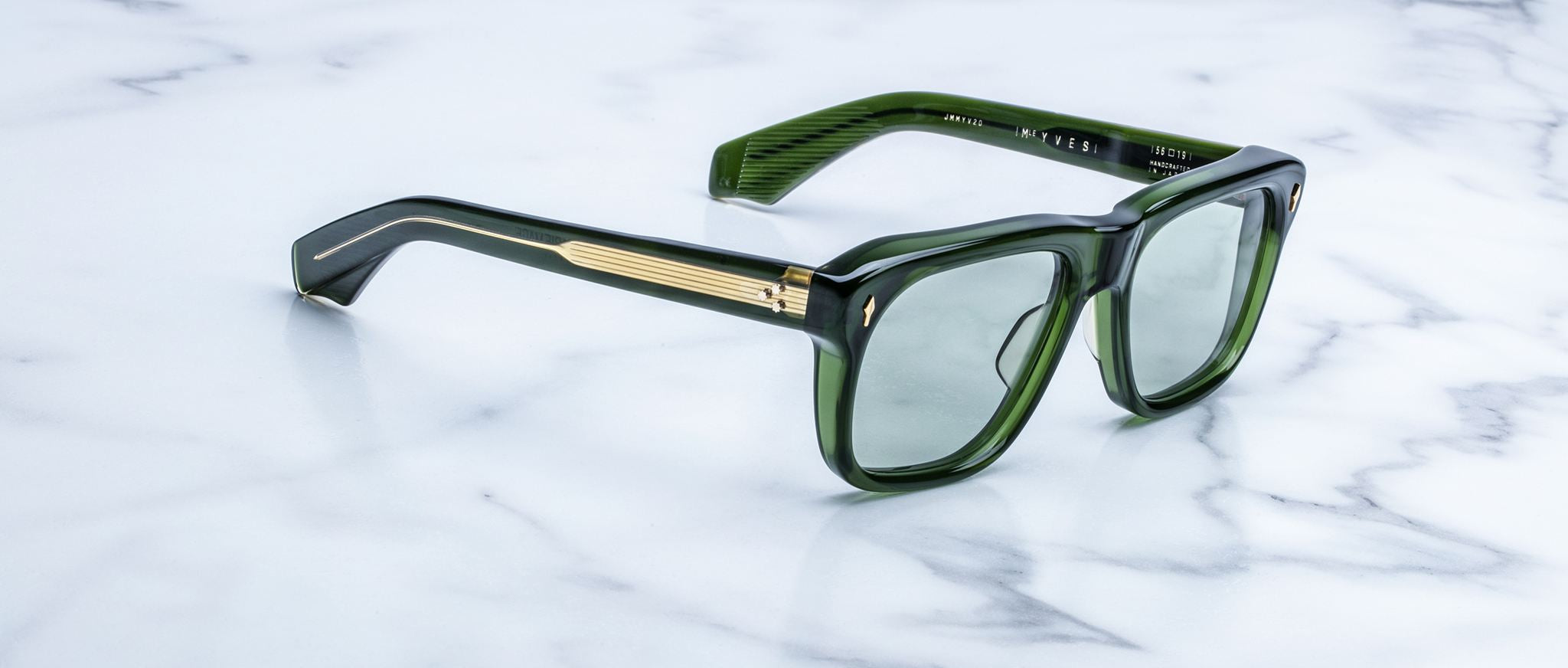 Jacques Marie Mage Yves sunglasses with green rectangular frames and gold accents, shown from the front on a white marble surface.