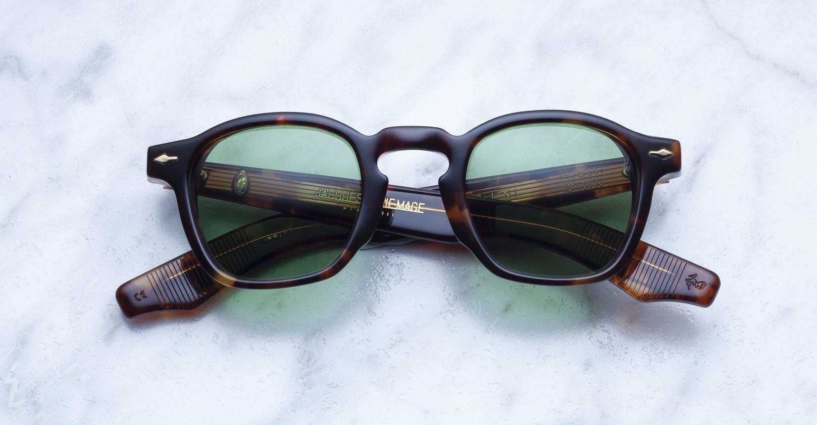 Jacques Marie Mage Zephirin square sunglasses in tortoiseshell acetate with green lenses are elegantly displayed on a light marble surface.