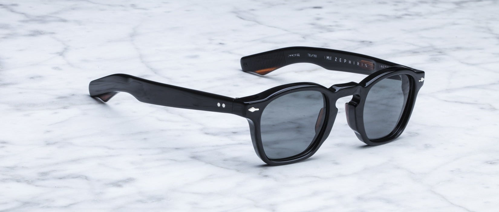 Jacques Marie Mage Zephirin black acetate sunglasses by Jacques Marie Mage rest on a white marble surface.