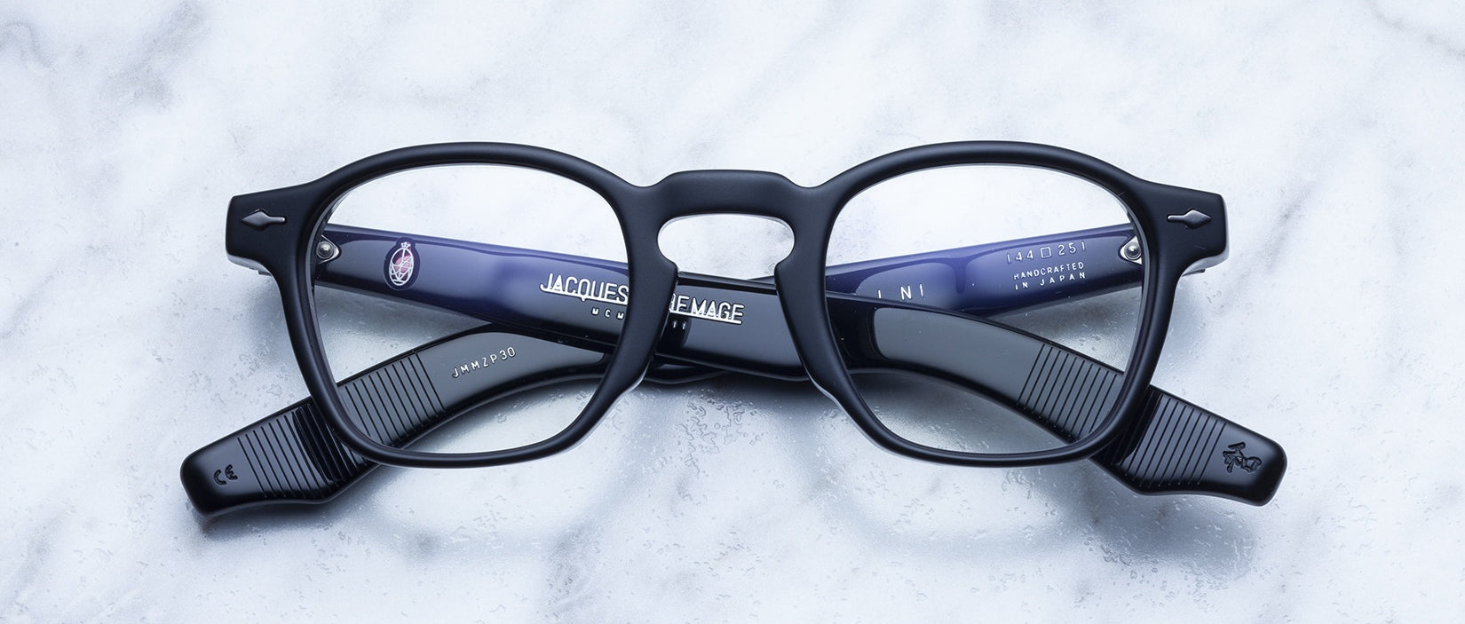Jacques Marie Mage Zephirin black rectangular eyeglass frames with textured arms are shown closed, face up on marble, highlighting the interior logos—limited edition eyewear handcrafted from premium acetate.