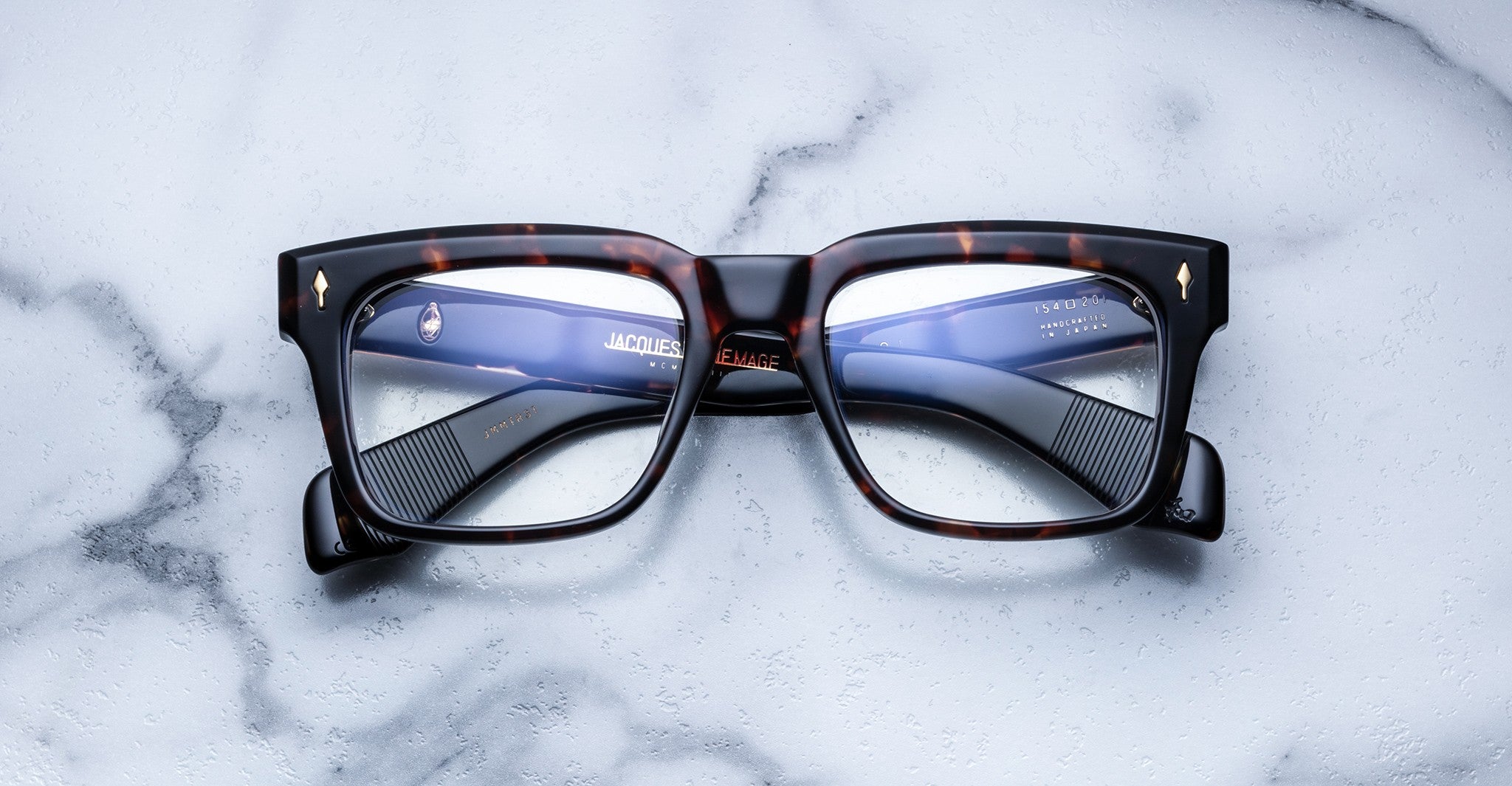A pair of Jacques Marie Mage Torino bold rectangular eyeglass frames in tortoiseshell handcrafted acetate by Jacques Marie Mage rests on a white marble surface.