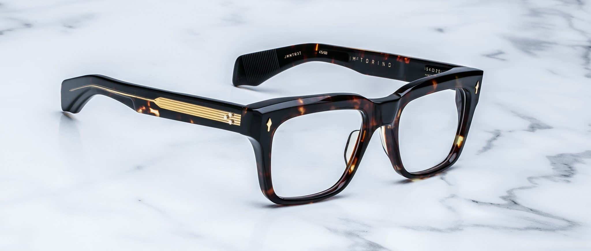 Jacques Marie Mage Torino eyeglasses: bold, handcrafted acetate frames in tortoiseshell with gold temple detailing, inspired by the iconic Jacques Marie Mage brand, elegantly displayed on a white marble surface.