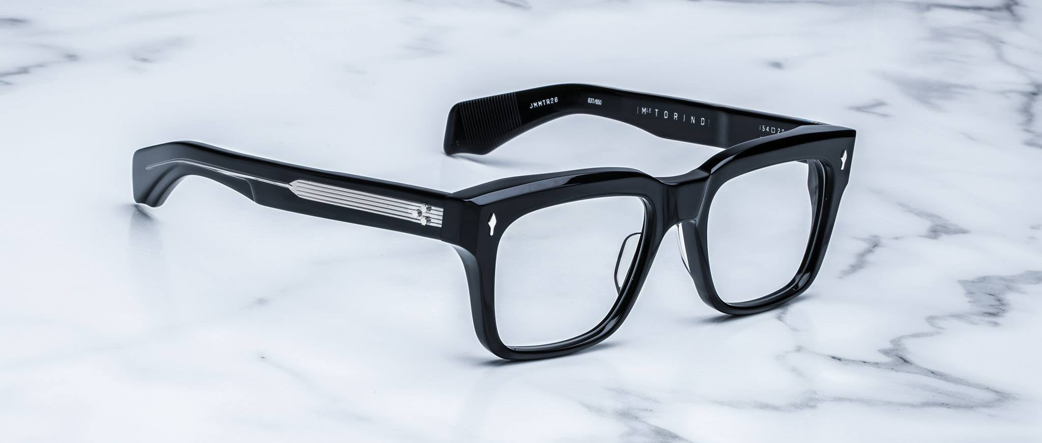 A pair of bold, handcrafted Jacques Marie Mage Torino rectangular acetate eyeglass frames is displayed on a white marble surface, showcasing the distinctive style of Jacques Marie Mage.
