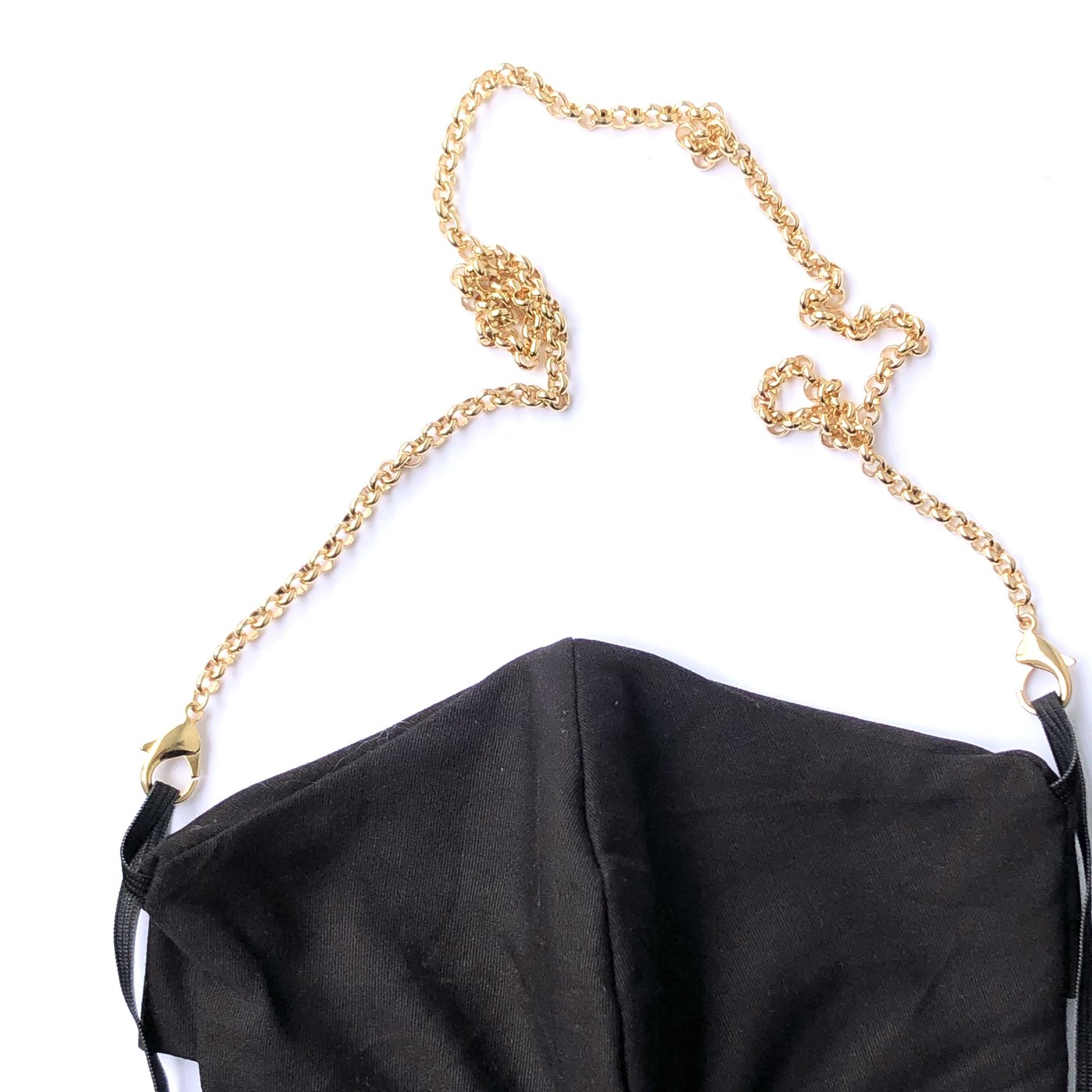A Rolo Necklace Chain for Face Masks, in gold, is attached to the mask's ear loops and elegantly arcs above a black mask on a white background, adding a chic jewelry accessory vibe.