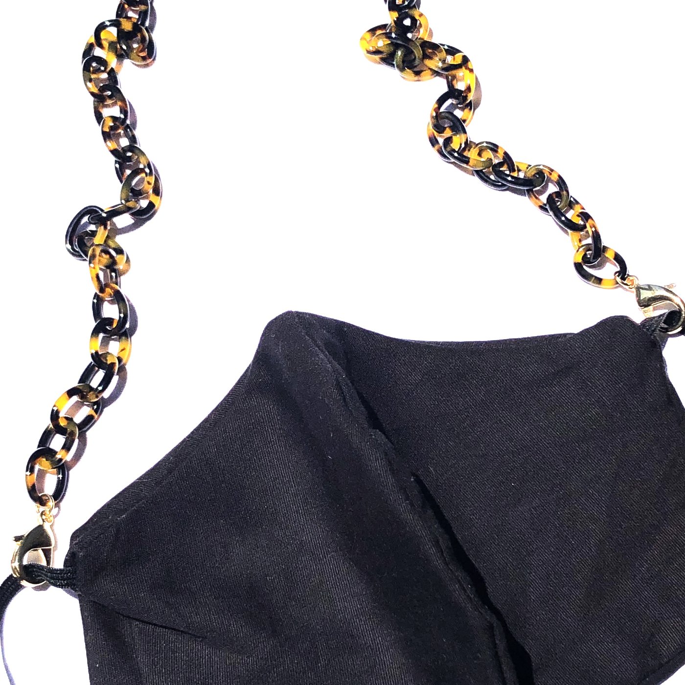 A black fabric face mask with the Small Link Necklace Chain for Face Masks, featuring a gold and black tortoiseshell pattern, used as a strap and displayed against a white background.