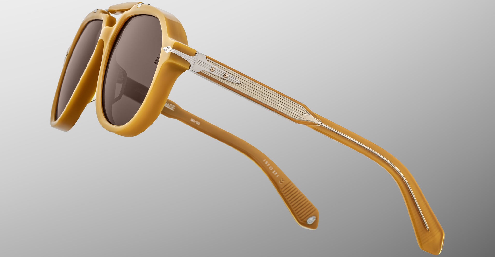 Close-up of Jacques Marie Mage 1991 sunglasses featuring stylish brown lenses, a thick amber-colored frame, and metal-accented arms, displayed against a neutral gradient background.