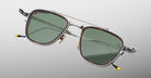 The Jacques Marie Mage 1992 sunglasses feature green-tinted lenses, silver metal frames, and yellow-accented temple tips, shown against a light gray background.