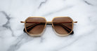 Jacques Marie Mage Aida sunglasses in gold-tone metal with a geometric square aviator shape, double bridge, and brown tinted lenses, front view on a neutral background.