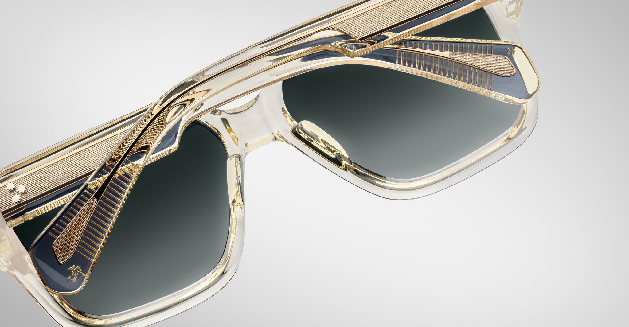 Close-up of Jacques Marie Mage Alfred sunglasses, featuring translucent gold frames, dark lenses, and detailed metallic accents on the temples, displayed from an angled view against a plain background.