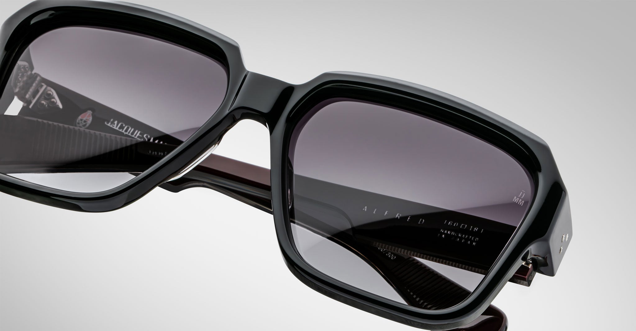 Close-up view of Jacques Marie Mage Alfred black rectangular sunglasses with dark tinted lenses and glossy finish. The inside of the temple arms is partially visible, showing subtle branding and product details.