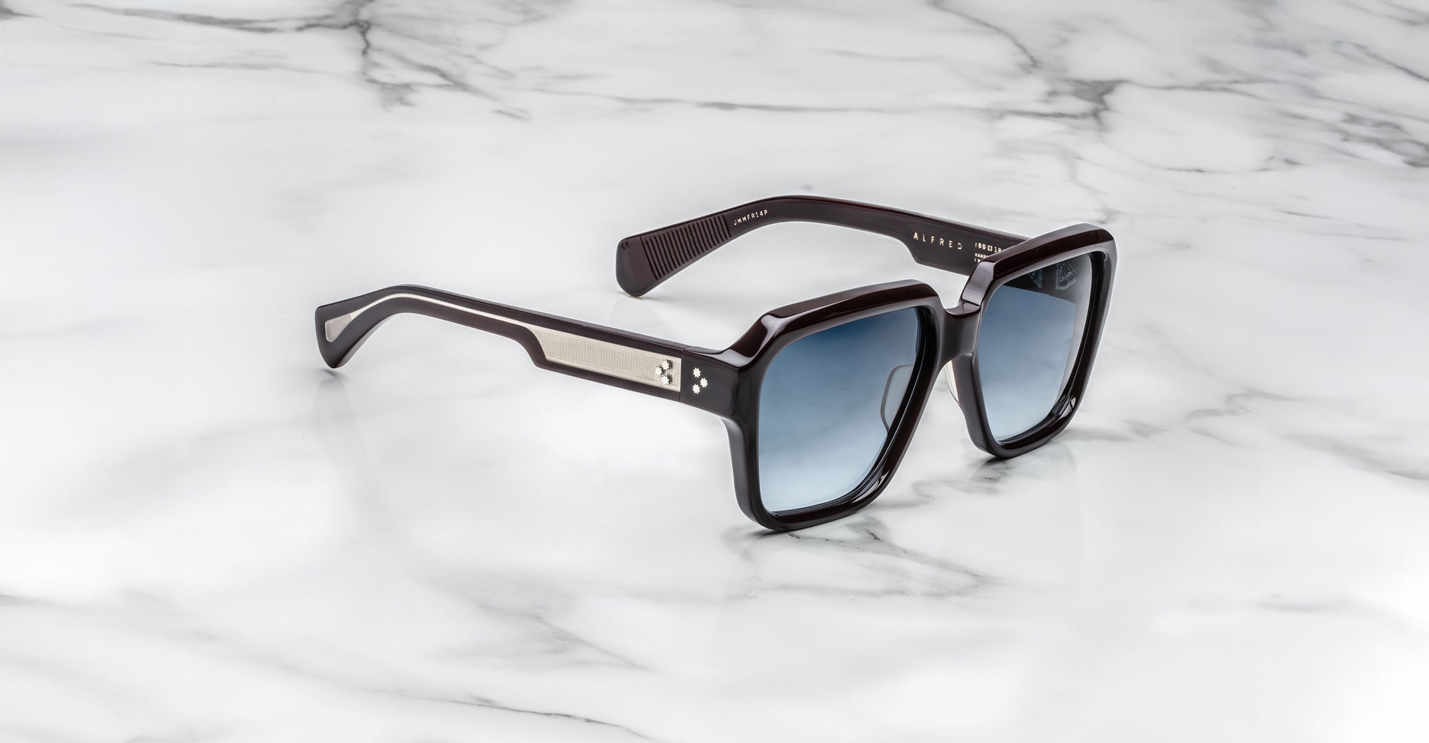 The Jacques Marie Mage Alfred features black square frames with blue gradient lenses and silver temple accents, displayed on a white marble surface.