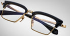 Close-up of Jacques Marie Mage Alin eyeglasses featuring black and gold frames, clear lenses, and detailed hinges. The arms display embossed text and intricate design elements, set against a plain light background.