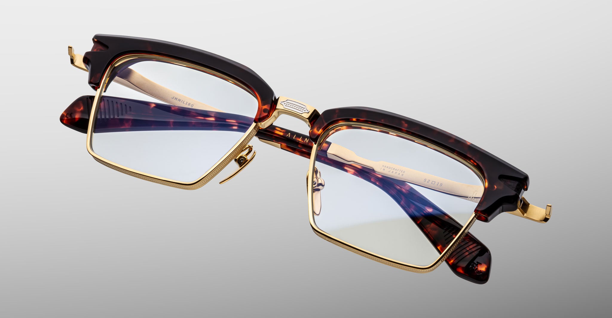 The Jacques Marie Mage Alin features rectangular gold metal frames with tortoiseshell acetate accents on the browline and arms, shown against a plain light gray background.