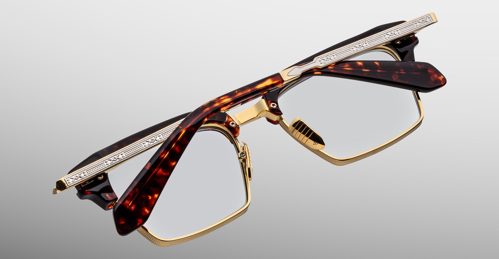 The Jacques Marie Mage Alin eyeglasses feature a gold metal frame with tortoiseshell-patterned browline and arms, plus engraved gold detailing, shown on a plain light gray background.