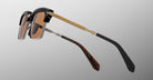 The Jacques Marie Mage Alin sunglasses feature brown tinted lenses, gold metal arms with etched patterns, black frame tops, and brown and black earpieces, displayed against a gradient gray background.
