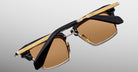 The Jacques Marie Mage Alin sunglasses feature brown lenses, black and gold frames, and engraved gold details on the top bar and temples, displayed against a plain light gray background.