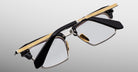 The Jacques Marie Mage Alin eyeglasses feature black arms, gold detailing on the top frame edge, clear lenses, and a bold angular design, displayed against a light gray background.