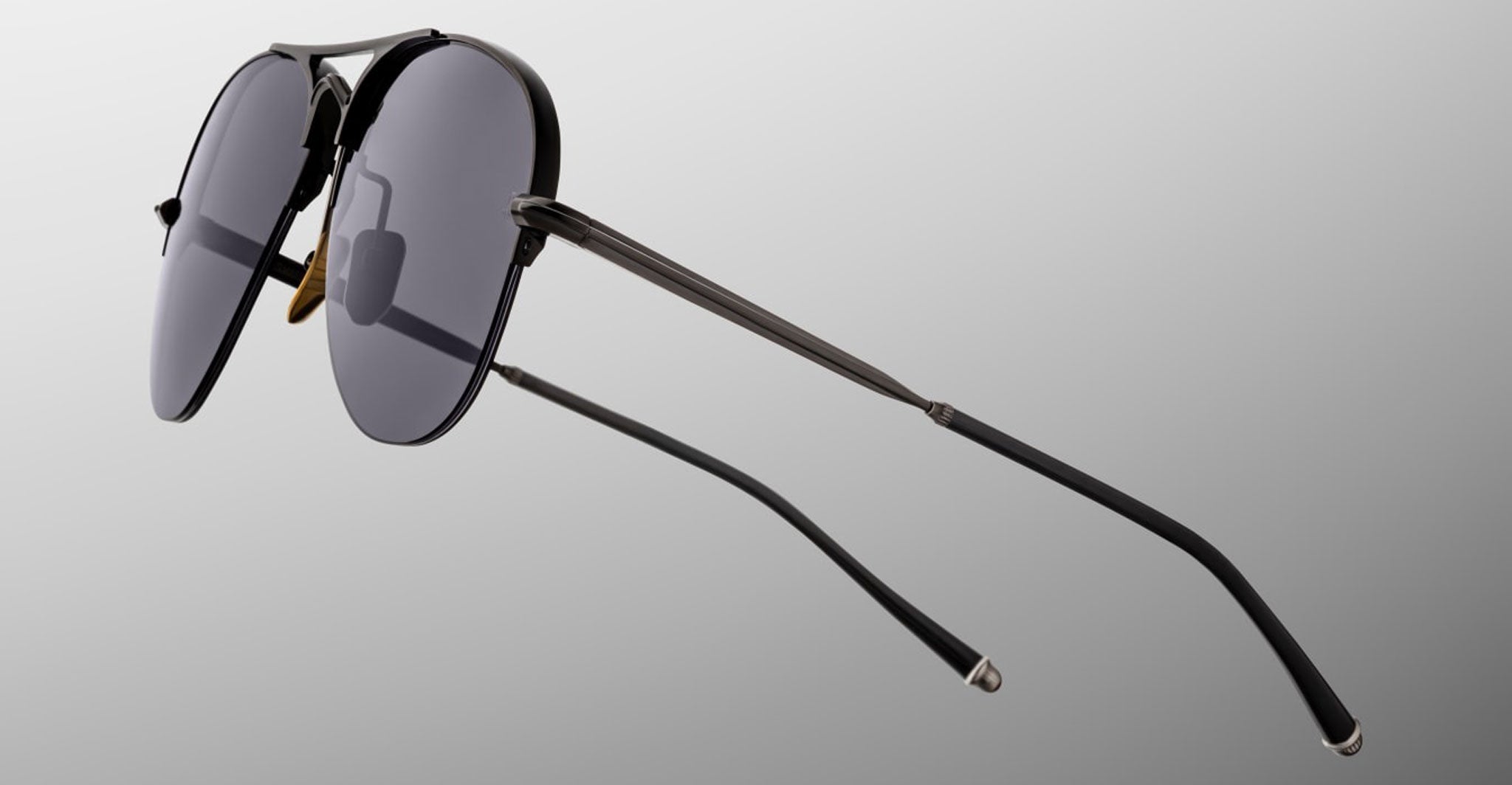 The Jacques Marie Mage Amelia is a pair of black aviator-style sunglasses featuring dark lenses and slender metal arms, displayed from the side and rear against a light gray background.