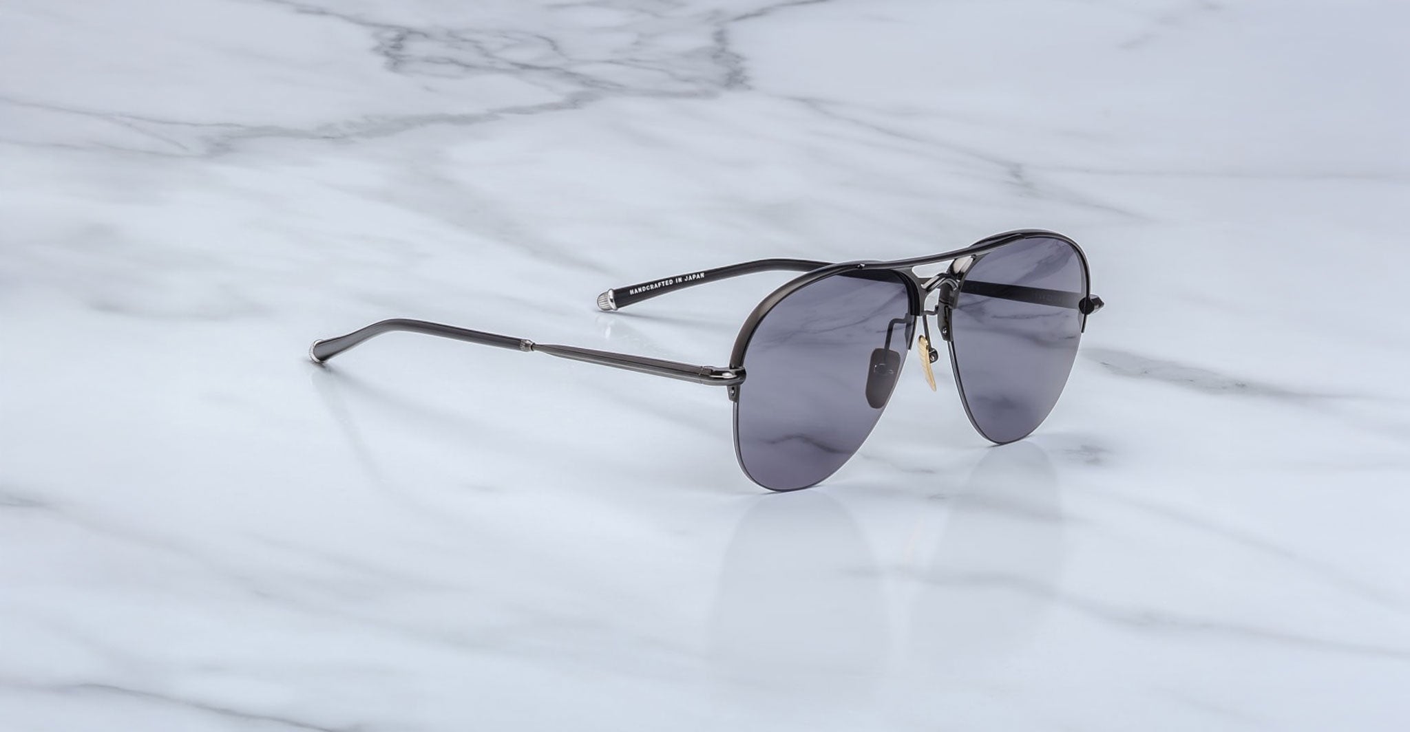 A pair of Jacques Marie Mage Amelia black aviator sunglasses with dark lenses rests on a white marble surface.
