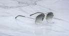 The Jacques Marie Mage Amelia aviator-style sunglasses with silver metal frames and gray gradient lenses rest on a white marble surface.