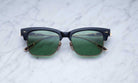 Jacques Marie Mage Apache sunglasses, black and gold frame with green lenses, viewed from above.