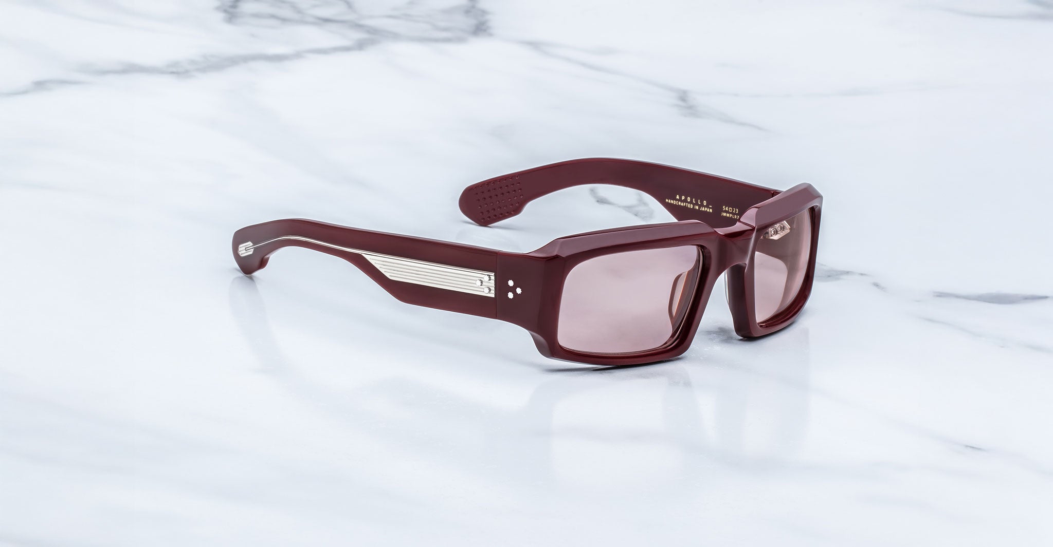 Jacques Marie Mage Apollo in Bordeaux Empire shown in angled side view, featuring a bold rectangular burgundy acetate frame, thick sculpted temples with exposed engraved metal core, triple dot rivets, signature arrowhead tips, and rose-tinted lenses.