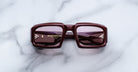 Front view of Jacques Marie Mage Apollo in Bordeaux Empire featuring a bold rectangular frame in deep burgundy acetate, thick sculpted rims, rose-tinted lenses, and hinge hardware visible through the lens.