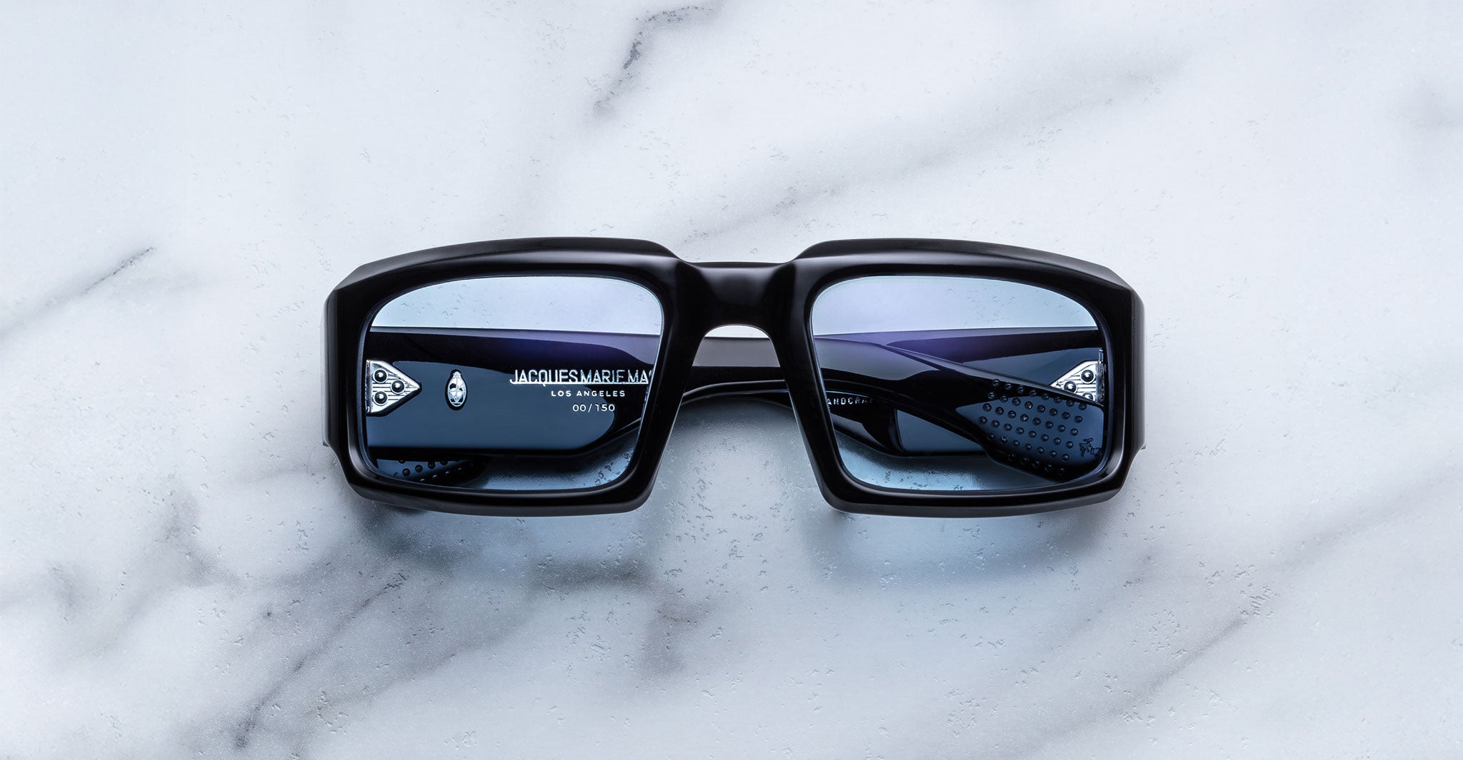 Front view of Jacques Marie Mage Apollo in Shadow featuring a bold rectangular black acetate frame, thick sculpted rims, blue-tinted lenses, and metal hinge details visible through the lens.