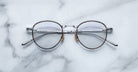A pair of Jacques Marie Mage Archibald round, silver-framed optical frame with thin metal arms rests on a white marble surface with grey veining.