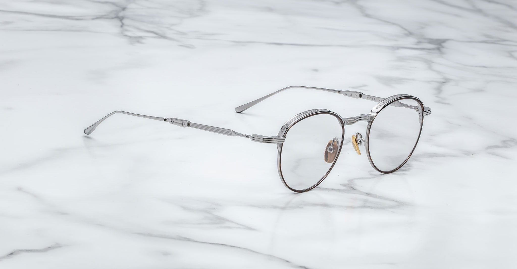 A pair of Jacques Marie Mage Archibald round, silver-framed optical frame with thin metal arms rests on a white marble surface with grey veining.