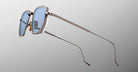 The Jacques Marie Mage Atkins sunglasses feature blue-tinted rectangular lenses, sleek silver metal frames, and slim elongated arms, displayed against a light gray background.