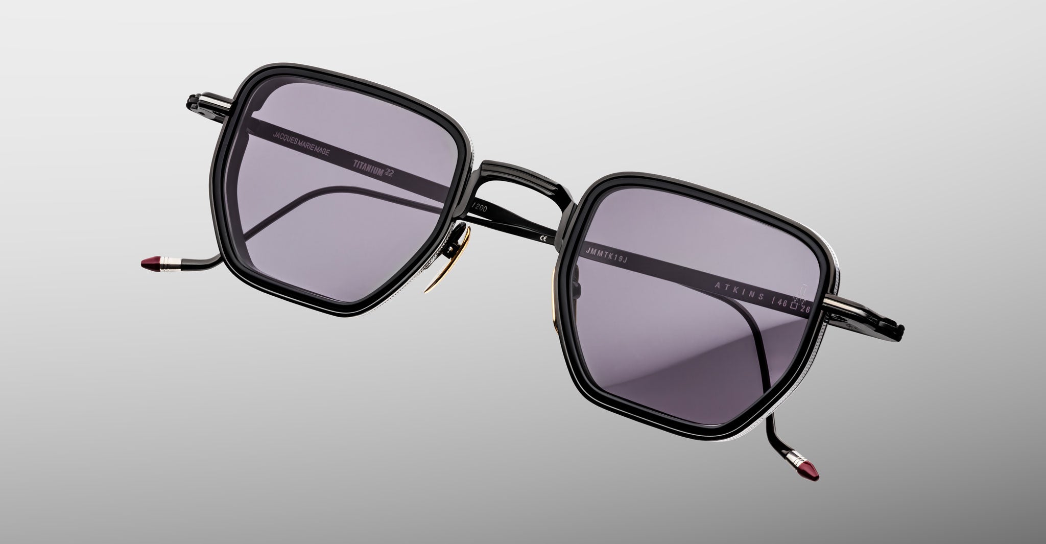 The Jacques Marie Mage Atkins are black, square-framed sunglasses with dark tinted lenses and slim metal arms, showcased on a light gray background—showing the essence of handcrafted Japanese eyewear.