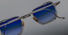 Close-up of Jacques Marie Mage Atkins eyeglasses, rectangular shape, blue-tinted lenses, silver frames, front view.