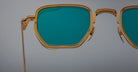 Close-up of Jacques Marie Mage Atkins sunglasses, gold frame with teal lenses, front angle.