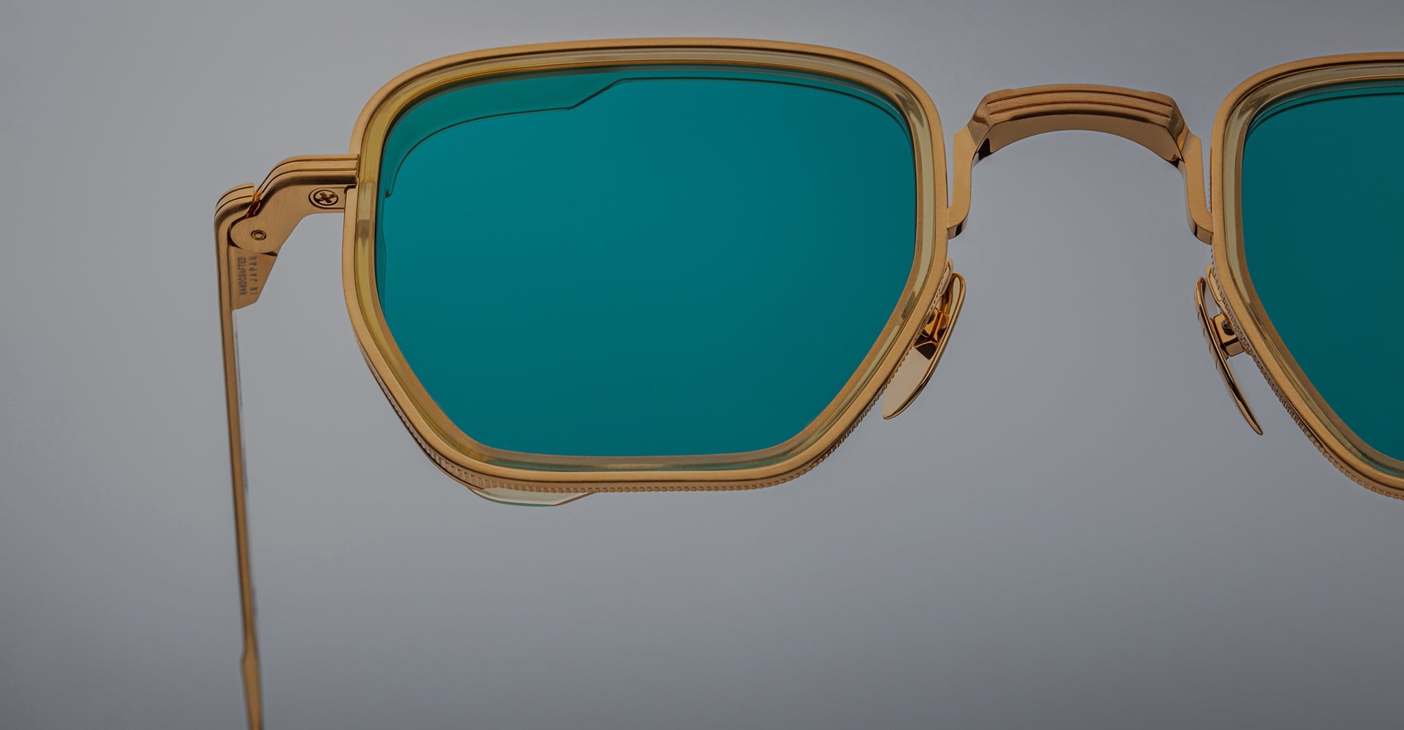 Close-up of Jacques Marie Mage Atkins sunglasses, gold frame with teal lenses, front angle.