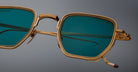 Close-up of Jacques Marie Mage Atkins sunglasses, square gold rims with teal lenses, viewed from the front.