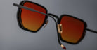 Close-up of Jacques Marie Mage Atkins black sunglasses, featuring red-orange lenses, shown from the front.