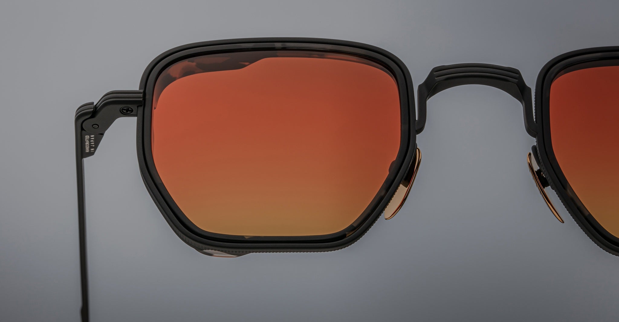 Close-up of Jacques Marie Mage Atkins geometric black sunglasses with orange-tinted lenses, shown from the front angle.